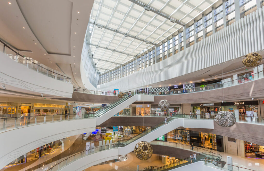 Vue intérieure d'un grand centre commercial moderne avec verrière et escalators, illustrant les besoins intensifs en électricité et en climatisation gérés par évole électricité.