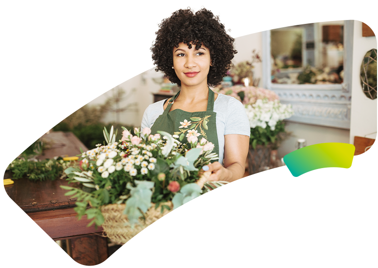 Gérante d'une boutique de fleuriste souriante avec une composition florale, illustrant les TPE et PME accompagnées par le service client 100% humain et basé en France d'évole électricité.